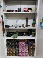 Zdjęcie przedstawia szarą szafę pancerną z półkami, na których znajduje się amunicja oraz inne akcesoria do broni.