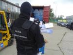 Funkcjonariusz celno-skarbowy trzymający nielegalne papierosy na tle kontenera
