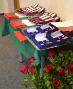Na stoliku leżą medale dla funkcjonariuszy i pracowników pomorskiej Krajowej Administracji Skarbowej oraz awanse. Z boku czerwone róże.
