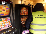 Dwóch funkcjonariuszy wkłada do samochodu automat do gry hazardowej.