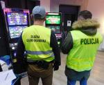 Funkcjonariusze Służby Celno-Skarbowej i Policji stoją przed maszynami do nielegalnych gier hazardowych.