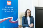 Minister Magdalena Rzeczkowska siedzi przy komputerze. Z lewej strony stoi roll-up z logo Krajowej Administracji Skarbowej.
