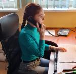 Młoda kobieta siedzi przy biurku i odbiera telefon