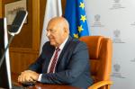 Minister Tadeusz Kościński siedzi przy biurku. Z tyłu baner z logo Ministerstwa Finansów.