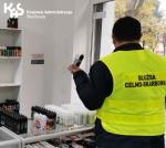Funkcjonariusz stoi tyłem w sklepie z papierosami elektronicznymi, w ręku trzyma zabezpieczone płyny. W lewym, górnym rogu logo KAS. 