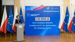 Minister rodziny i polityki społecznej Marlena Maląg stoi przed mikrofonem. Po obu stronach stoją flagi Polski i Unii Europejskiej. Po środku stoi baner z Polskim Ładem.