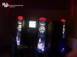 Trzy automaty do gier hazardowych stoją w ciemnym pomieszczeniu. W lewym górnym rogu logo Krajowej Administracji Skarbowej.