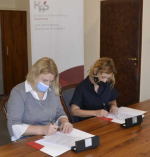 Dwie osoby siedzą przy stole i podpisują dokumenty. 