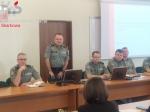 Sala konferencyjna. Przedstawiciele Pomorskiego Urzędu Celno-Skarbowego w Gdyni siedzą w mundurach przy stole. Na stole leżą laptopy. Po prawej stronie widać ekran z wyświetlaną prezentacją.  W lewym górnym rogu logo Krajowej Administracji Skarbowej.