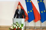 Szef KAS Bartosz Zbaraszczuk przemawia podczas konferencji na tle flag Polski i UE 