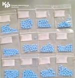 Kilkanaście torebek foliowych z niebieskimi tabletkami w środku. W lewym, górnym rogu logo Krajowej Administracji Skarbowej.