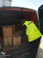 Funkcjonariusz Urzędu Celno-Skarbowego ładuje w kartonach alkohol do samochodu